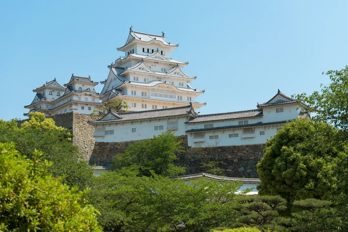The white keep of Himeji Castle above green trees in May on a day trip from Kyoto